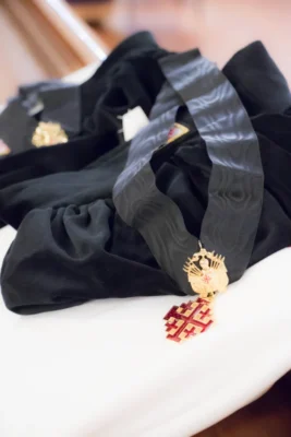The Jerusalem Cross insignia of a Knight of the Order, suspended from a black marbled silk ribbon and worn around the neck at liturgical ceremonies.